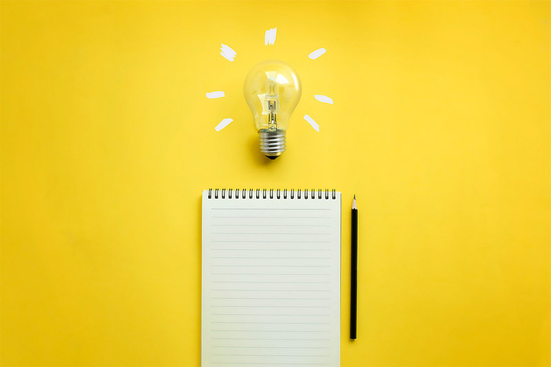 Schreibblock mit Stift und einer Glühbirne auf gelbem Hintergrund