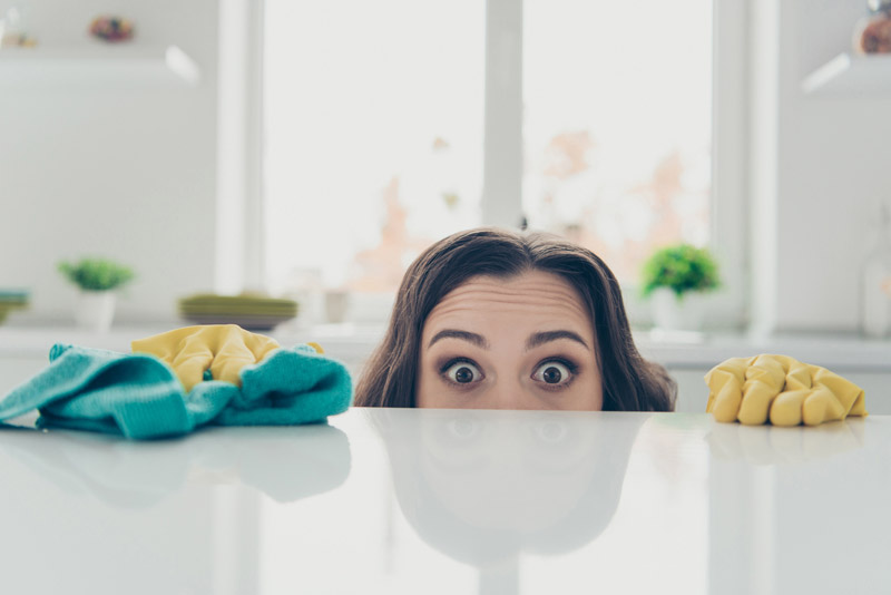 Eine Frau schaut über einen weißen Tisch und hat ein grünes Reinigungstuch in einer Hand