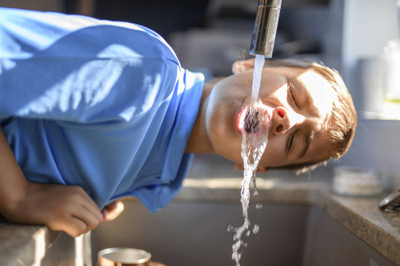 kleiner Junge trinkt Wasser aus dem Wasserhahn